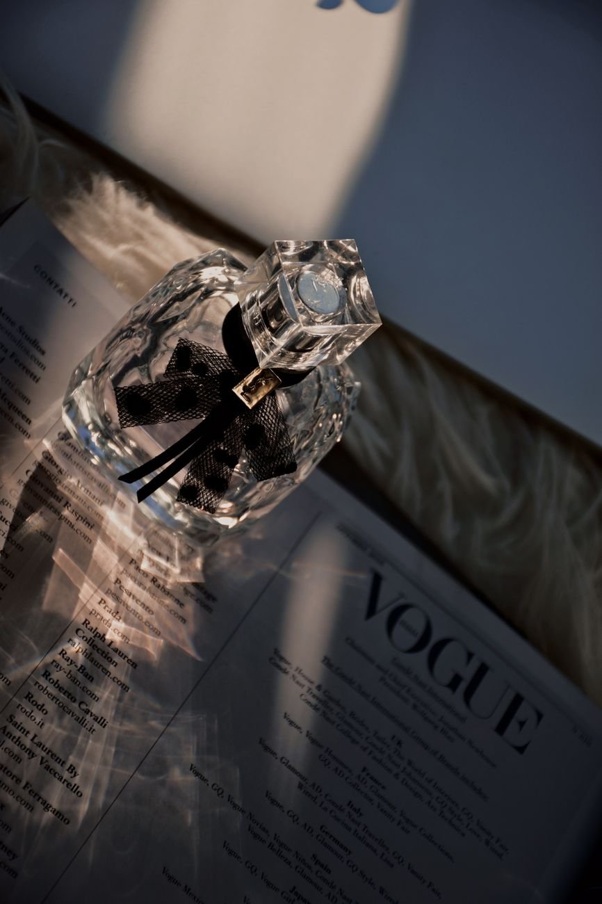 A crystal perfume bottle casting shadows on an open magazine, with stylish lighting.