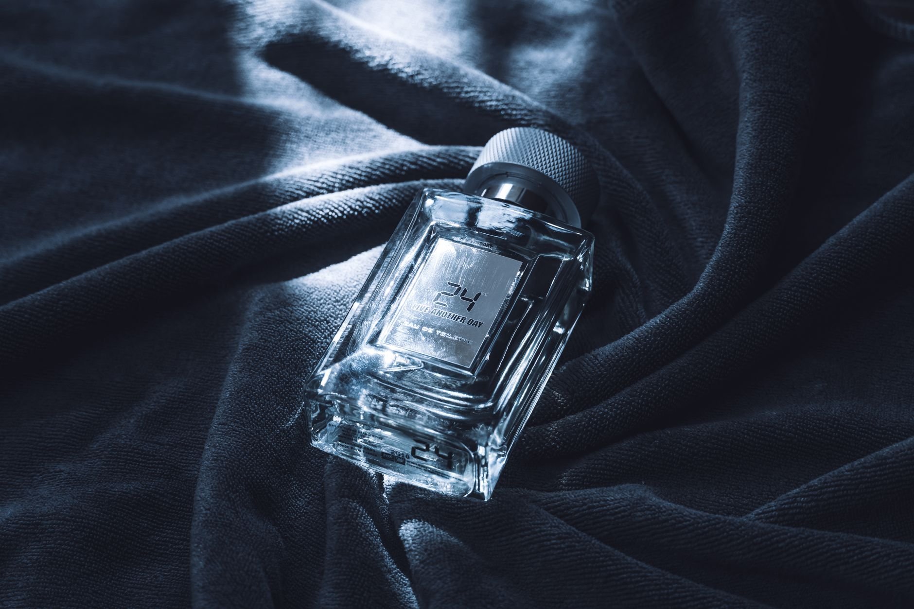 Elegant glass perfume bottle on dark fabric, capturing luxury and style in a moody setting.